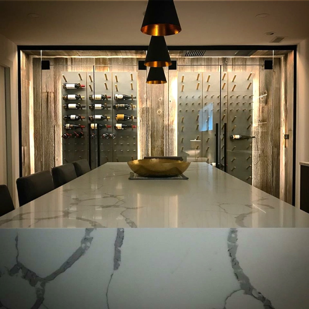 Wine tasting island beside a glass-enclosed cellar with STACT Premier Concrete & Gold wine racks.